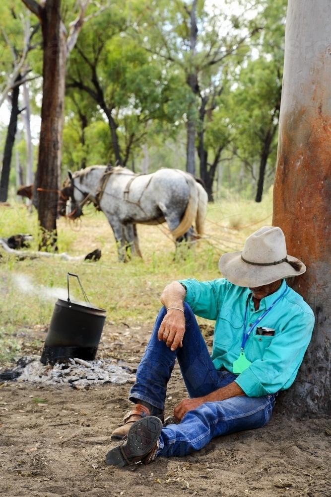 A cattle drover in his forties naps against a tree at morning tea. - Australian Stock Image