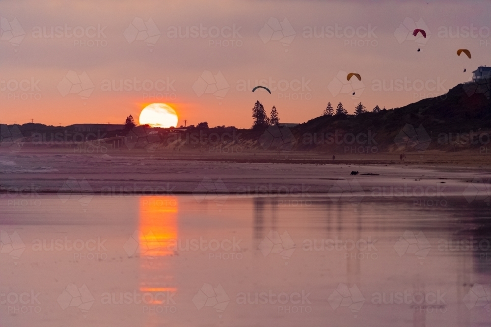 A colourful sunset reflecting on a wet beach with parasailers in the sky - Australian Stock Image