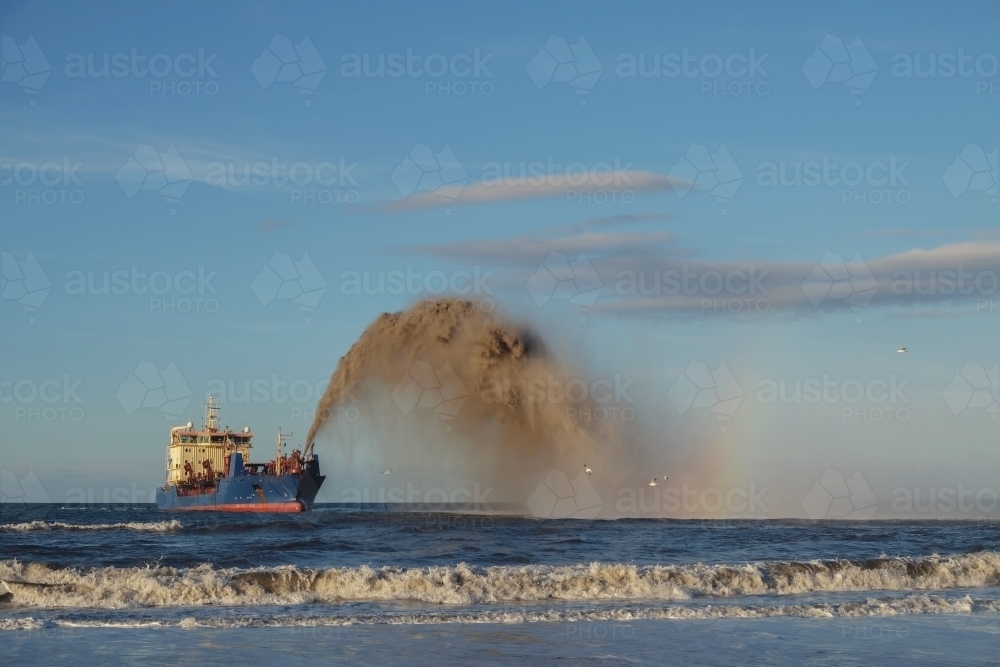 A dredging ship rainbowing sand into the ocean - Australian Stock Image