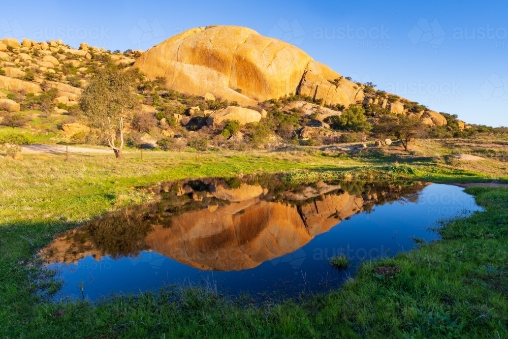 A large granite mountain in late evening light reflected in a dam - Australian Stock Image