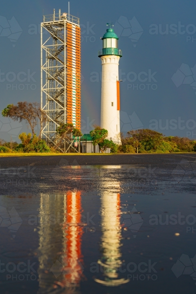 A light and signal tower highlighted against a dark sky and reflected in a puddle - Australian Stock Image