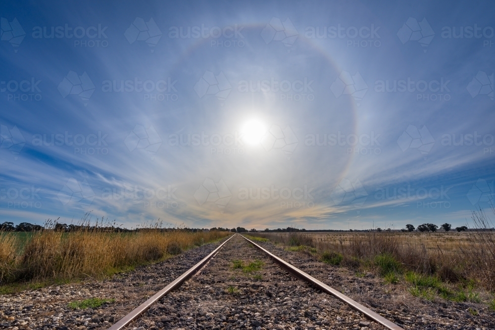 A solar halo low in the sky over receding railway tracks - Australian Stock Image