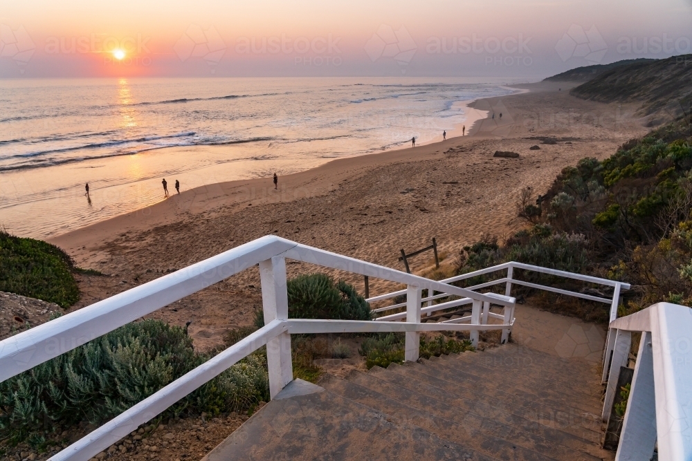 A staircase leading down to sandy beach with people walking at sunset - Australian Stock Image