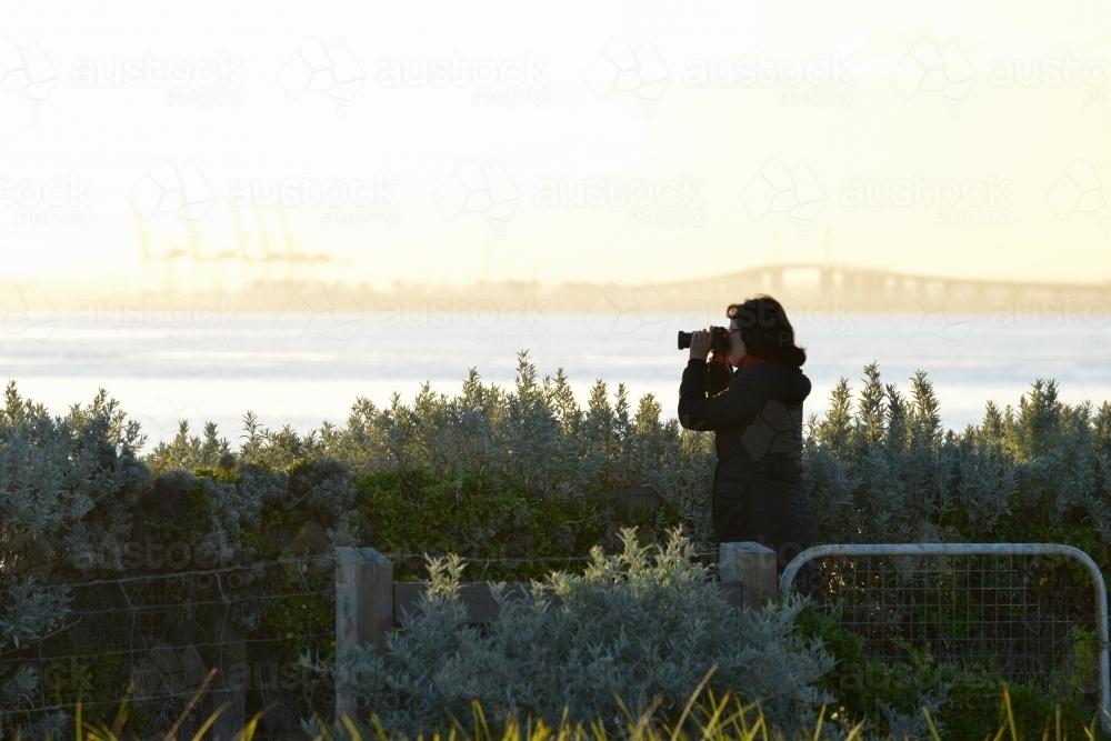 A woman takes photos at sunset near the bay - Australian Stock Image