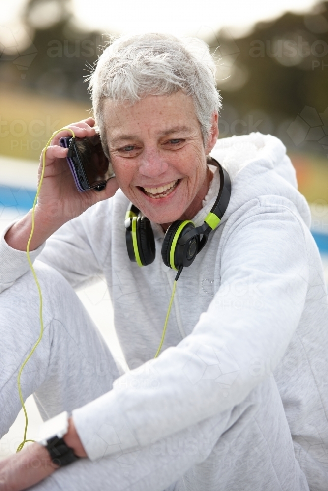 Active senior lady listening to music with headphones - Australian Stock Image