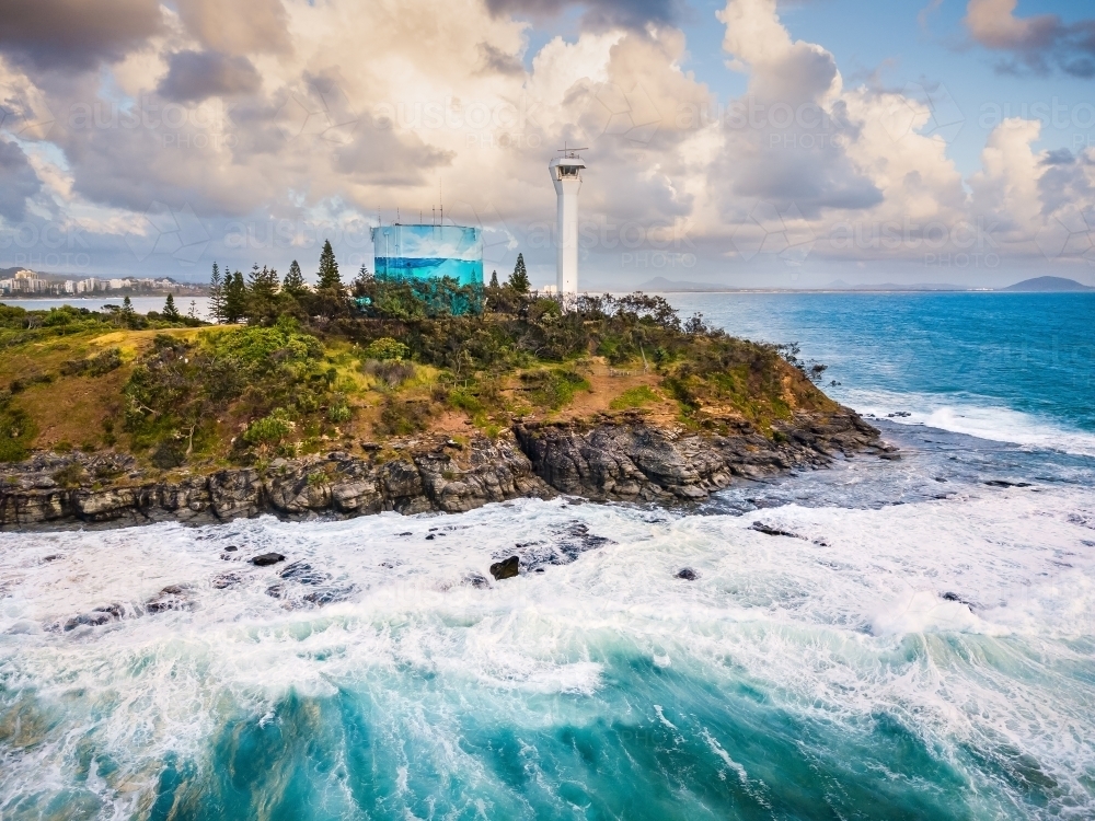 Aerial view of a lighthouse and a water tank on a clifftop above crashing waves - Australian Stock Image