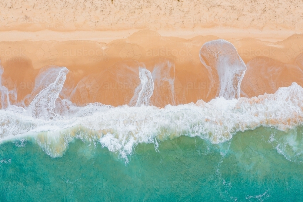 Aerial view of wave crashing and leaving patterns on a wide sandy beach - Australian Stock Image