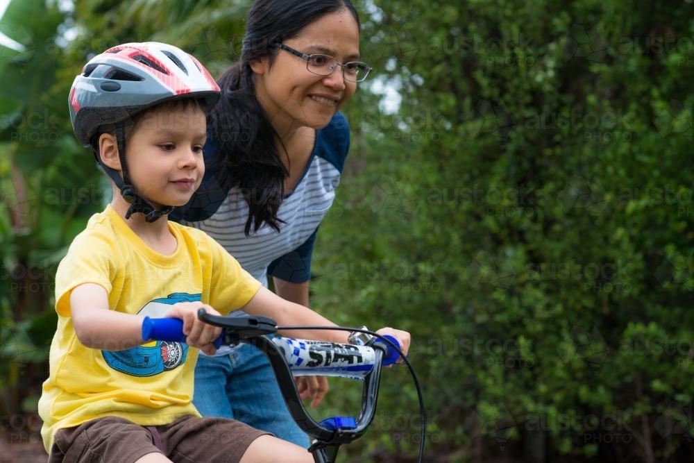Asian mum teaching her mixed race boy to ride a bike - Australian Stock Image
