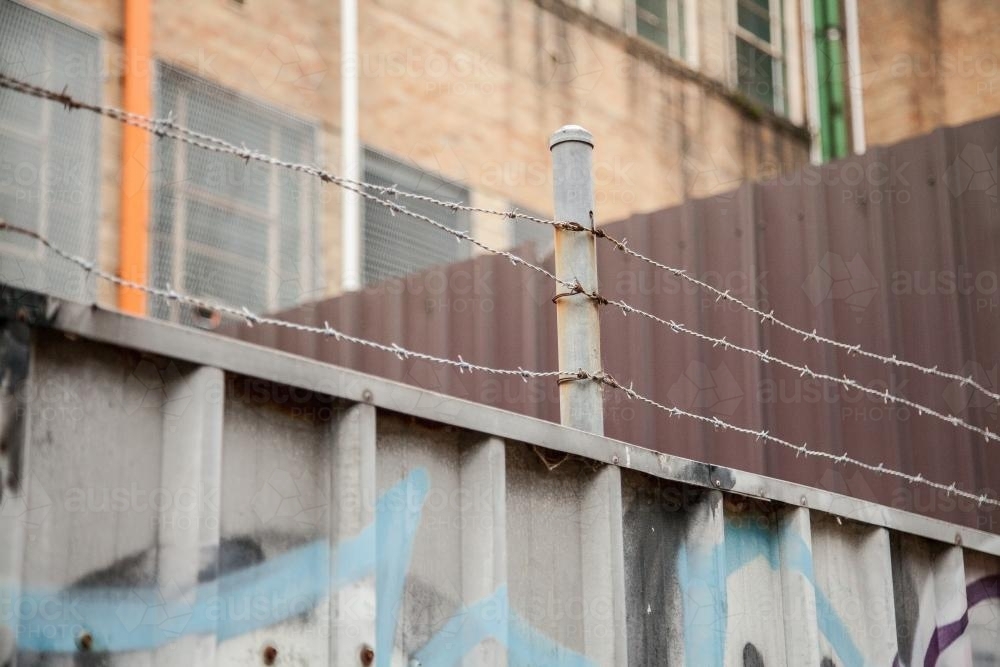 Barbed wire on top of a corrugated iron fence at the end of an alley - Australian Stock Image