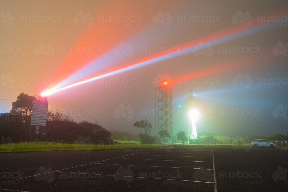 Beams of light from a lighthouse and beacon tower on a dark foggy night - Australian Stock Image