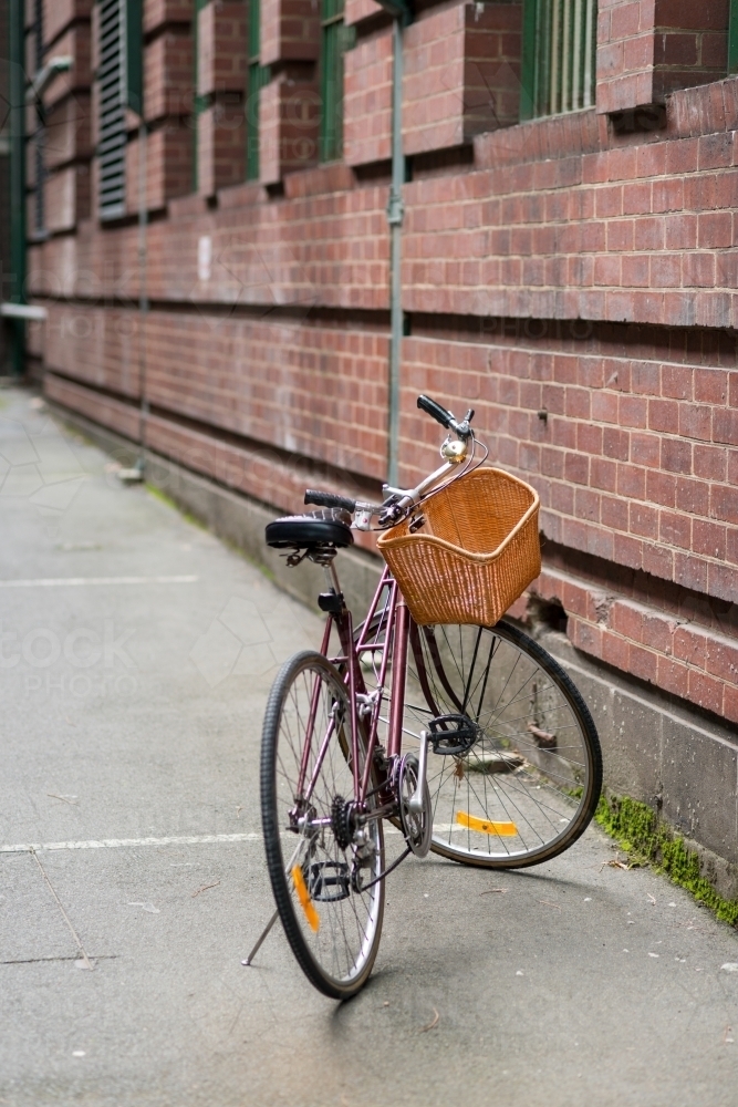 Bicycle with a woven basket parked next to a brick wall - Australian Stock Image