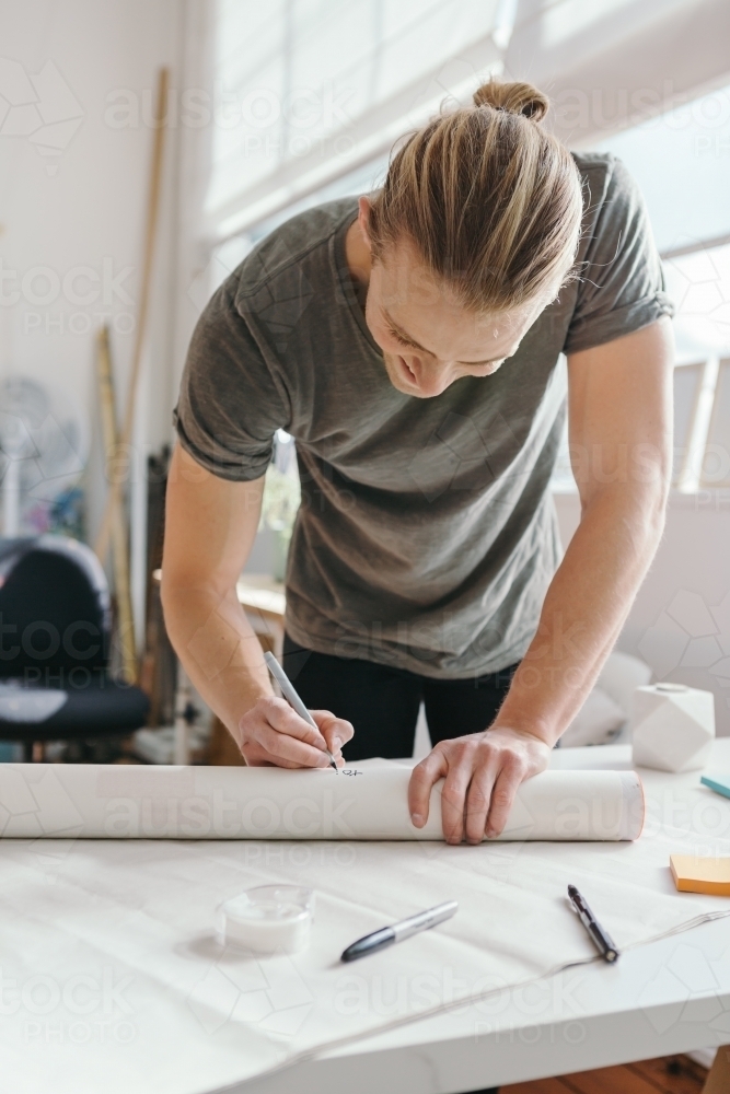 Blond guy addressing a mailing tube in an artist studio - Australian Stock Image