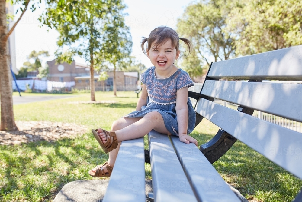 Child smiling on park bench wearing a blue dress - Australian Stock Image