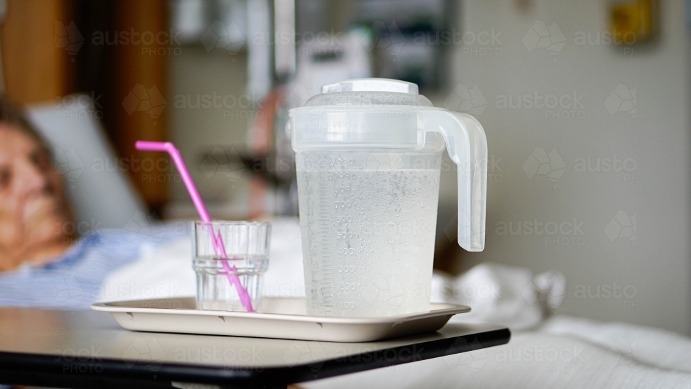 Close of hospital water jug and glass with patient in background - Australian Stock Image
