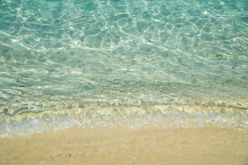Close up of blue sea water and a small wave bubbling onto a beach - Australian Stock Image