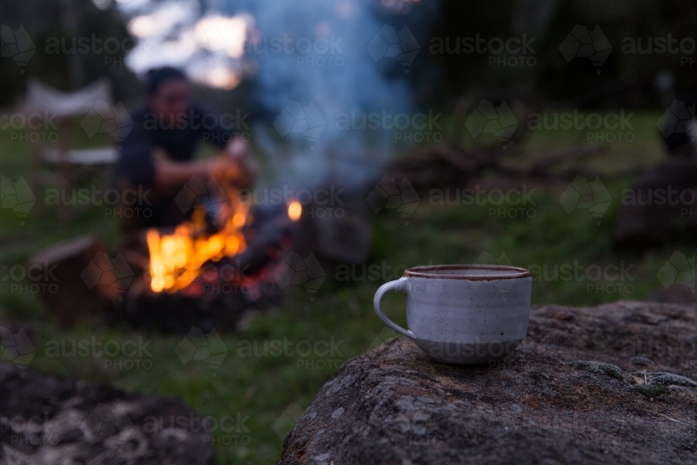 Close up of tea with man tending to campfire in background on rural property - Australian Stock Image