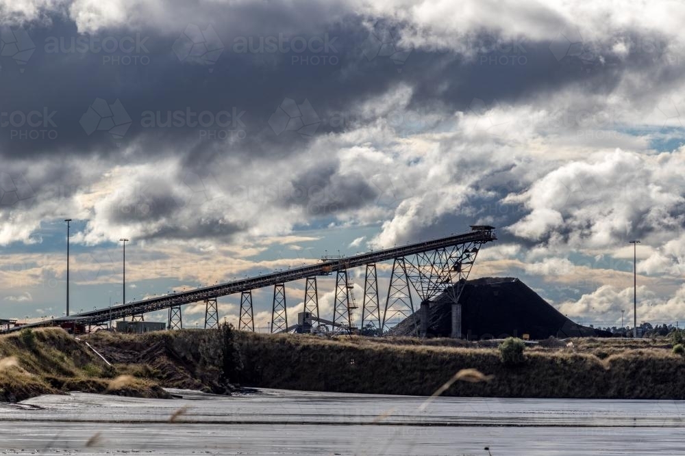 Coal conveyor and stockpile in the distance against dark clouds - Australian Stock Image