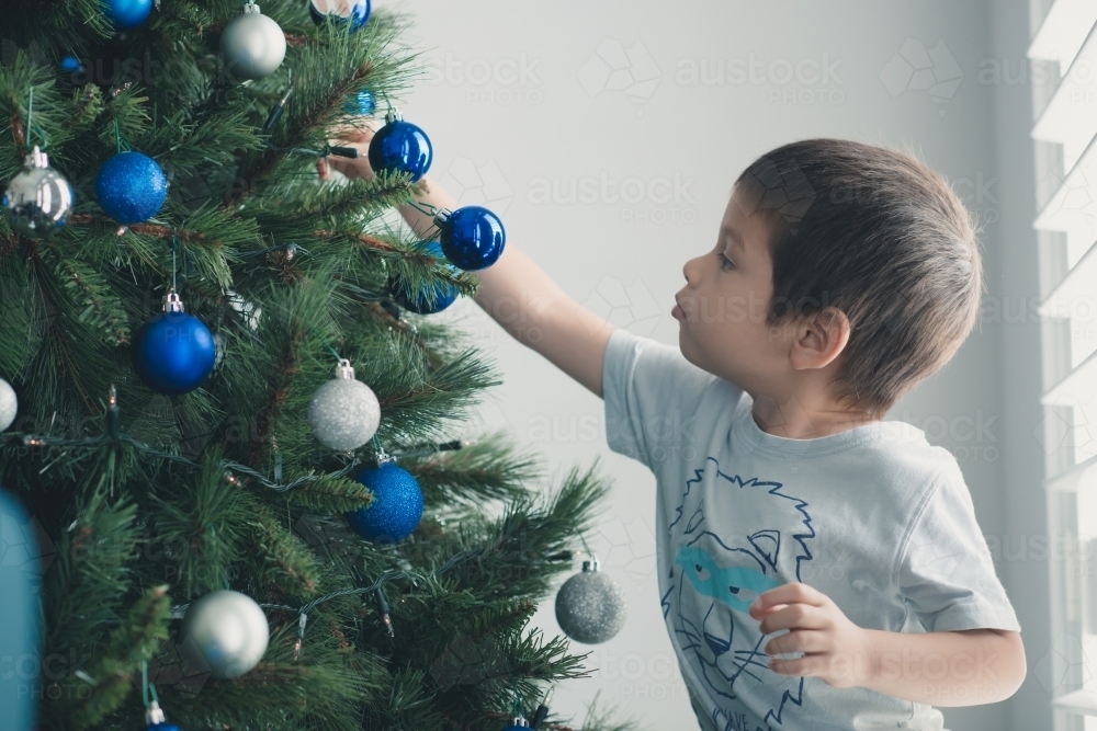 Cute mixed race boy hanging decorations on Christmas tree - Australian Stock Image