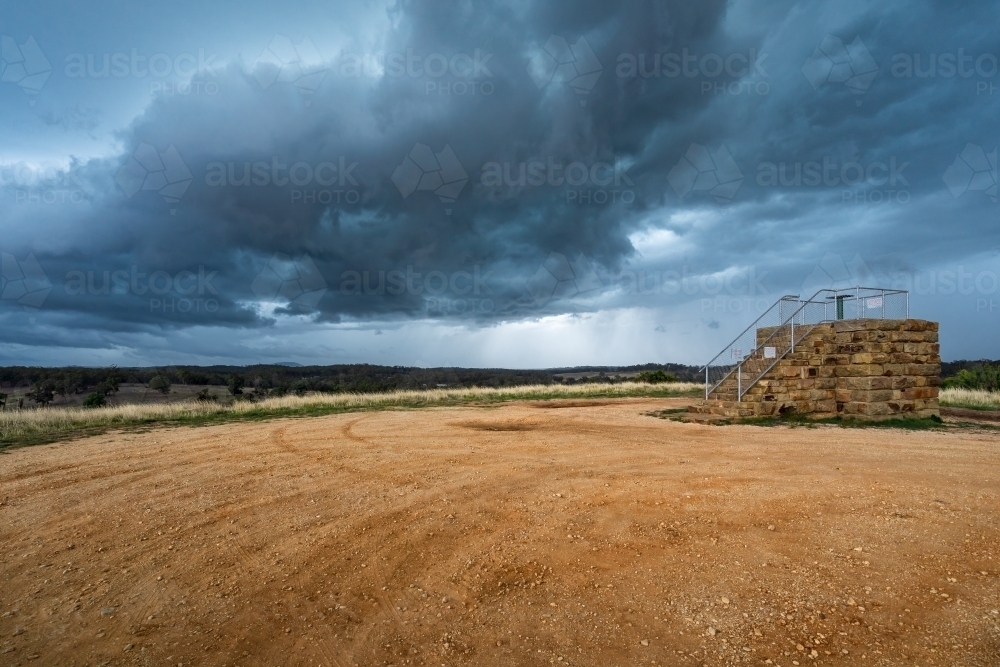Dark cloud formations over a raised stone lookout platform - Australian Stock Image