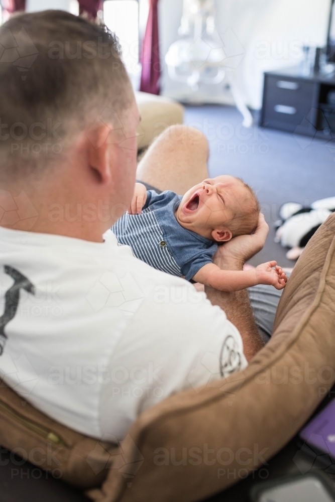 Father holding newborn baby boy stretching and yawning - Australian Stock Image