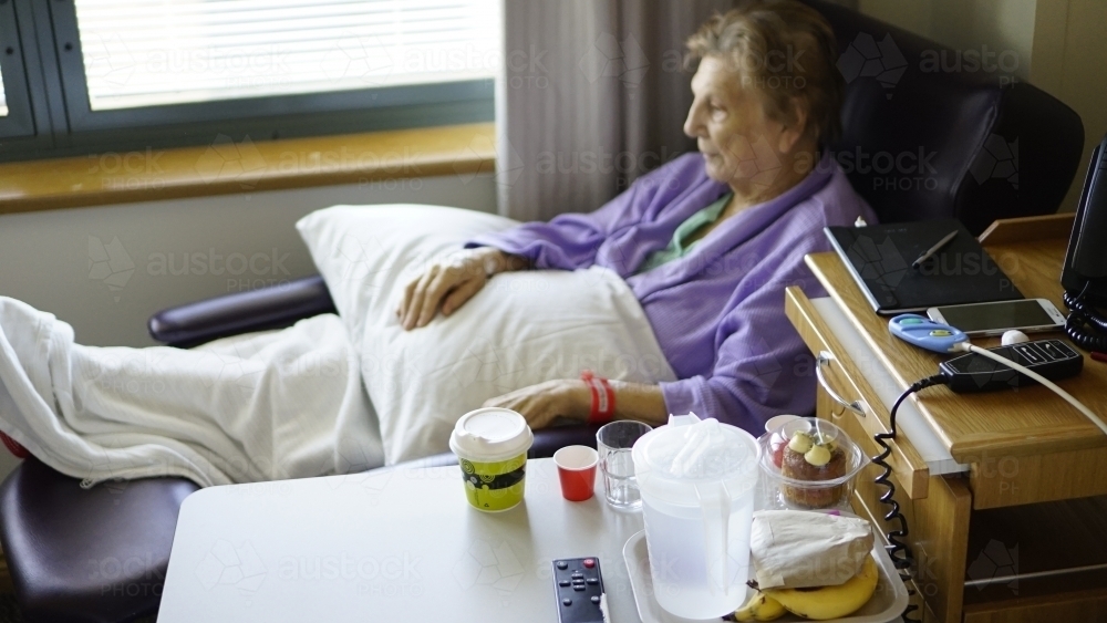 Female patient sitting in hospital chair by window - Australian Stock Image