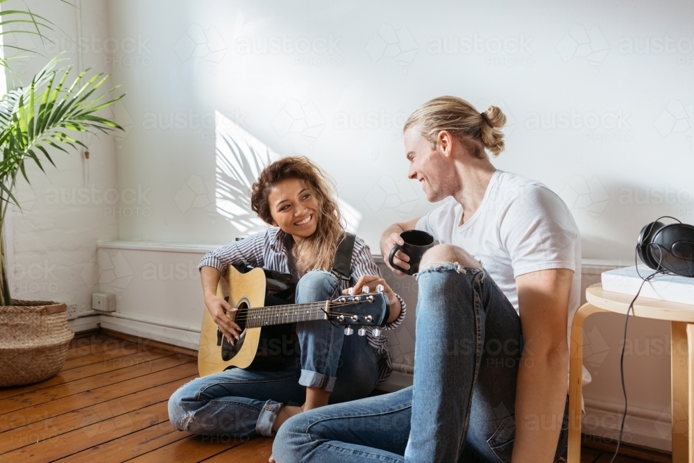 Female playing guitar sitting on the floor with her partner - Australian Stock Image