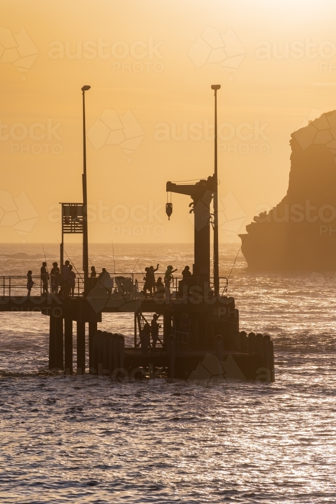 Fishermen and sightseers on a jetty in front of a golden sky - Australian Stock Image