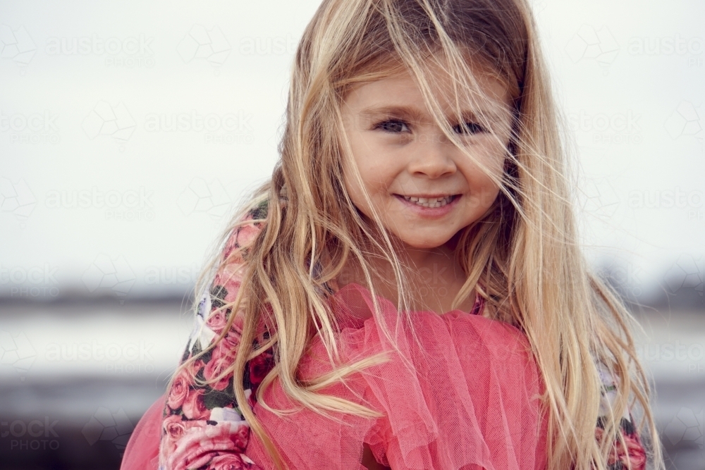 Five year old sitting on beach with windy hair - Australian Stock Image