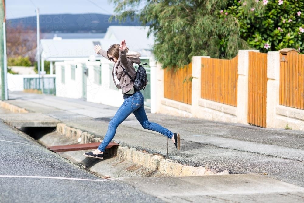 Girl jumping across gutter in street - Australian Stock Image