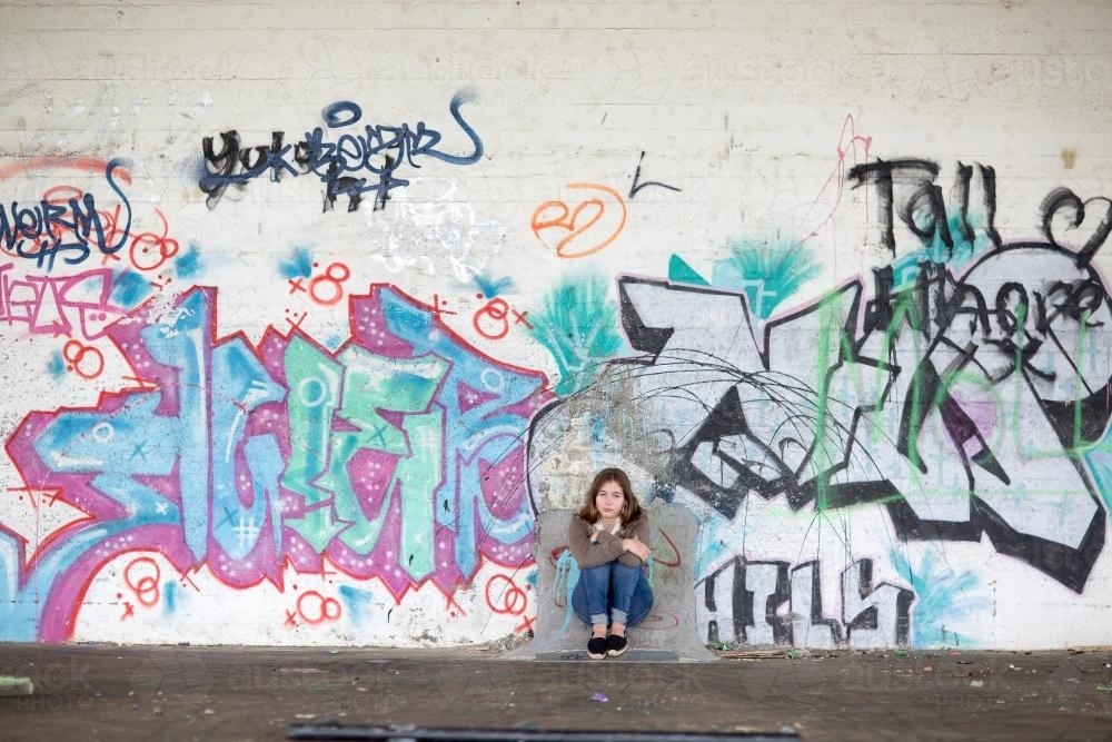 Girl sitting with graffiti on wall - Australian Stock Image