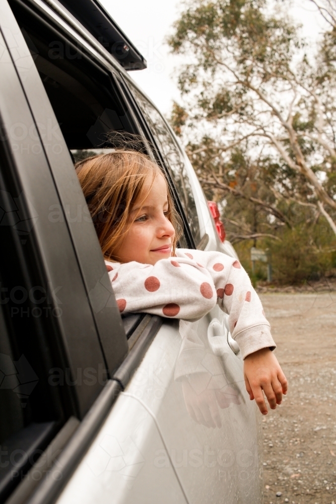 Girl traveling through country parked at rest stop looking out car window - Australian Stock Image