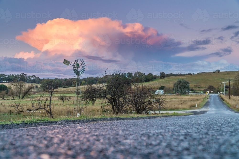 Ground level view of a large pink thunderhead above farmland and a country road - Australian Stock Image