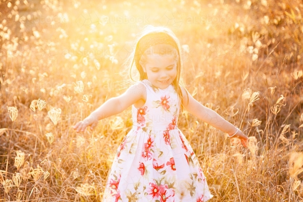 Happy little girl laughing and spinning in sunlit grass - Australian Stock Image