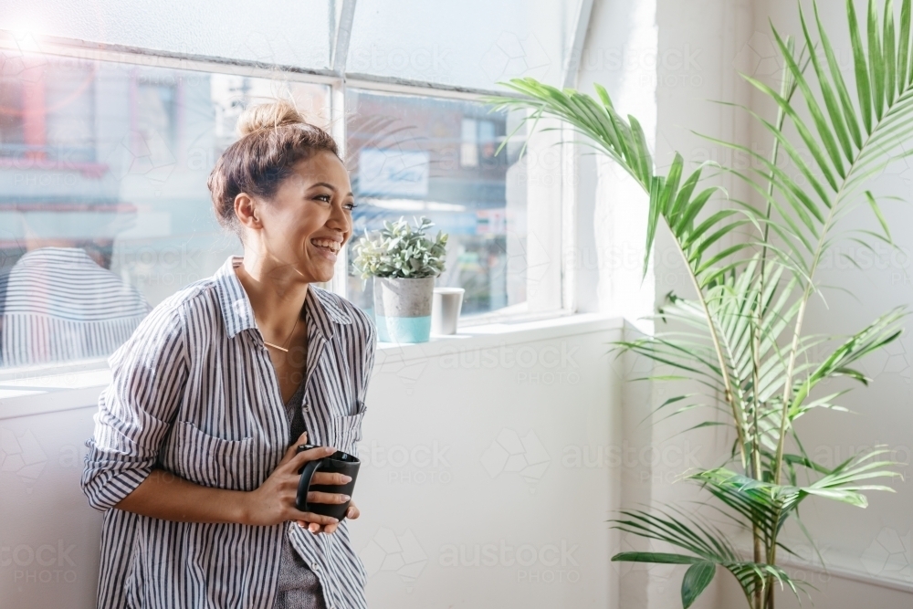 Happy young girl with a coffee mug laughing at something off camera - Australian Stock Image