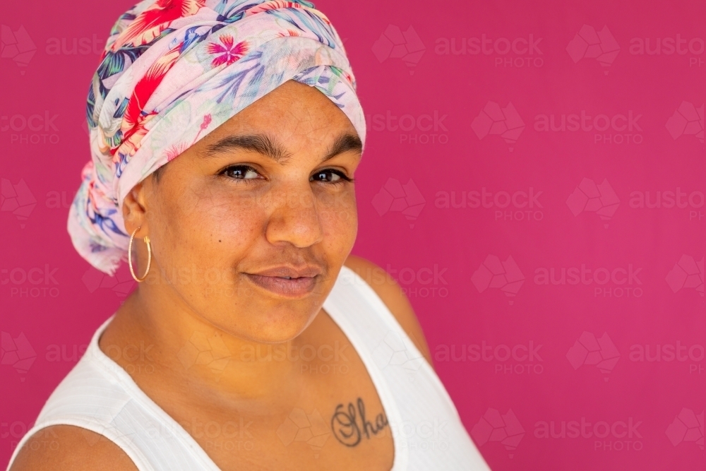 head and shoulders of woman wearing floral scarf wrapped on head against pink background - Australian Stock Image