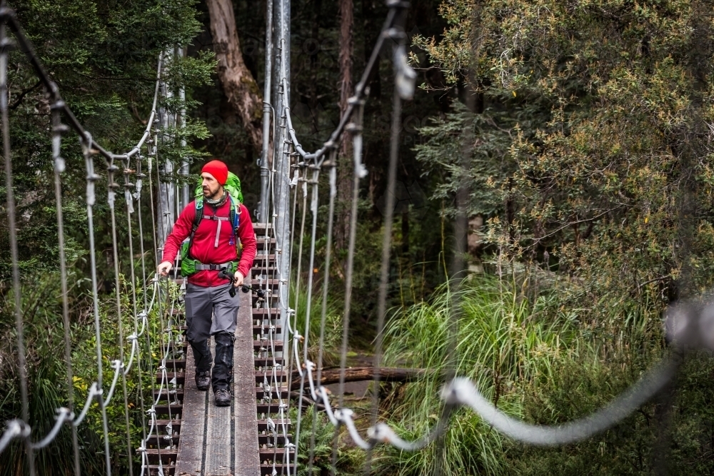 Hiker crossing a suspension bridge - Australian Stock Image