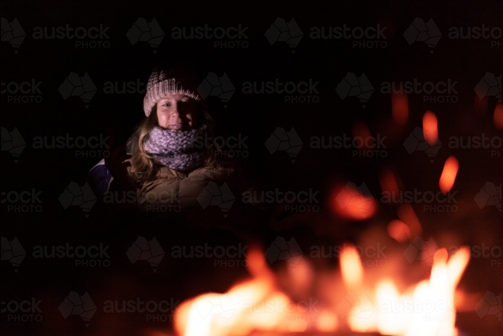 horizontal shot of a woman wearing winter clothes with camp fire blurred in the foreground - Australian Stock Image