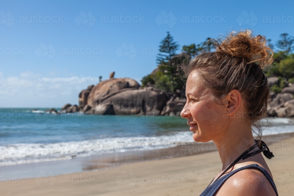 horizontal side view shot of woman looking from a far by the beach with waves, trees and mountains - Australian Stock Image
