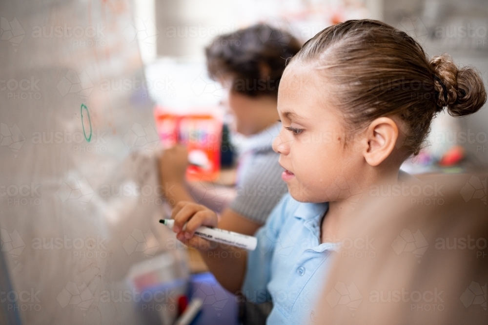 Indigenous primary school student writing on a whiteboard - Australian Stock Image