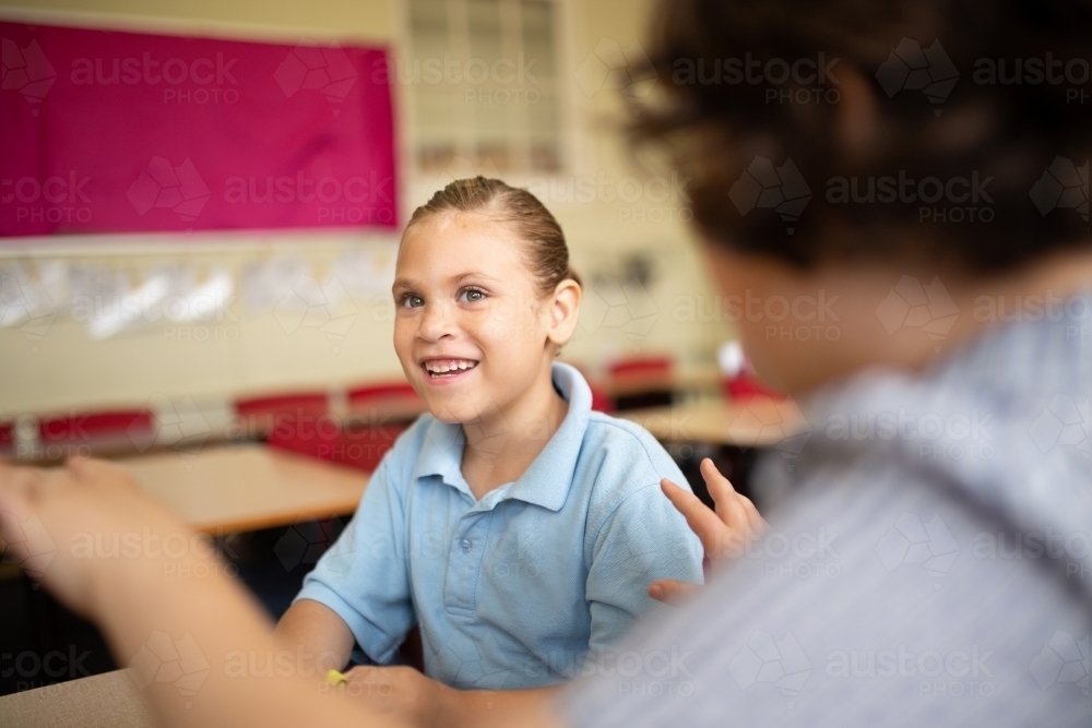 Indigenous student thinking and smiling with a friend in a classroom - Australian Stock Image