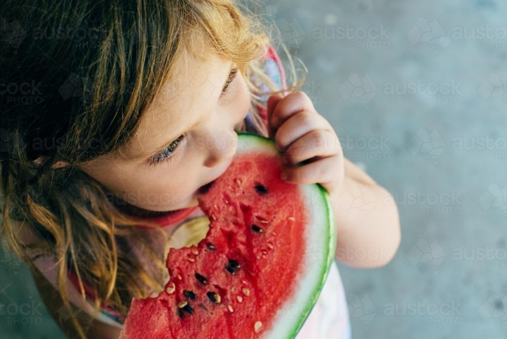 Little girl looking away, eating watermelon - Australian Stock Image