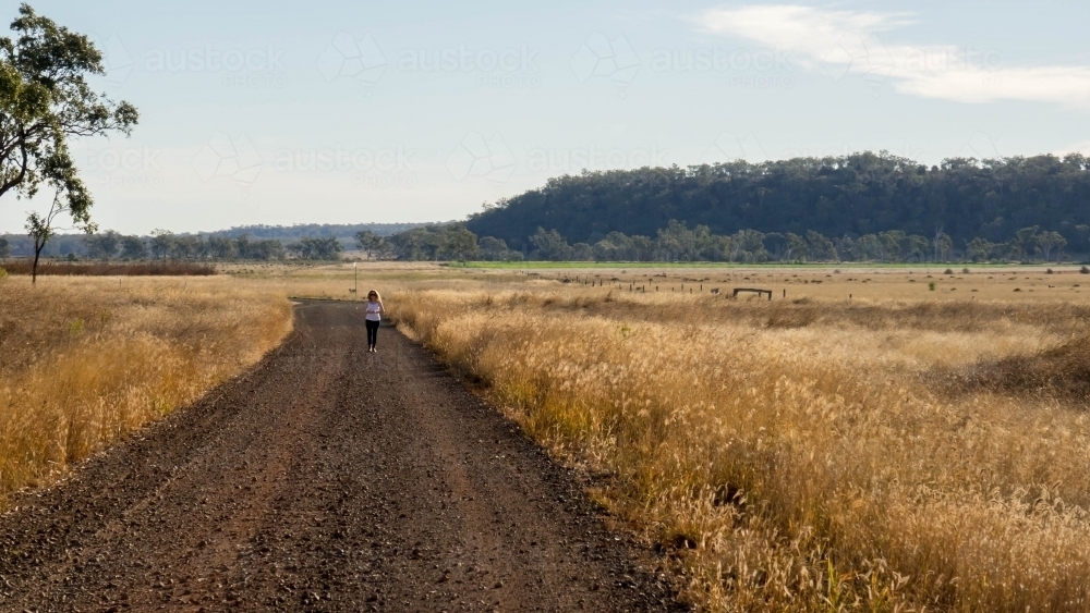 Long view of girl standing on dirt country road in the countryside - Australian Stock Image