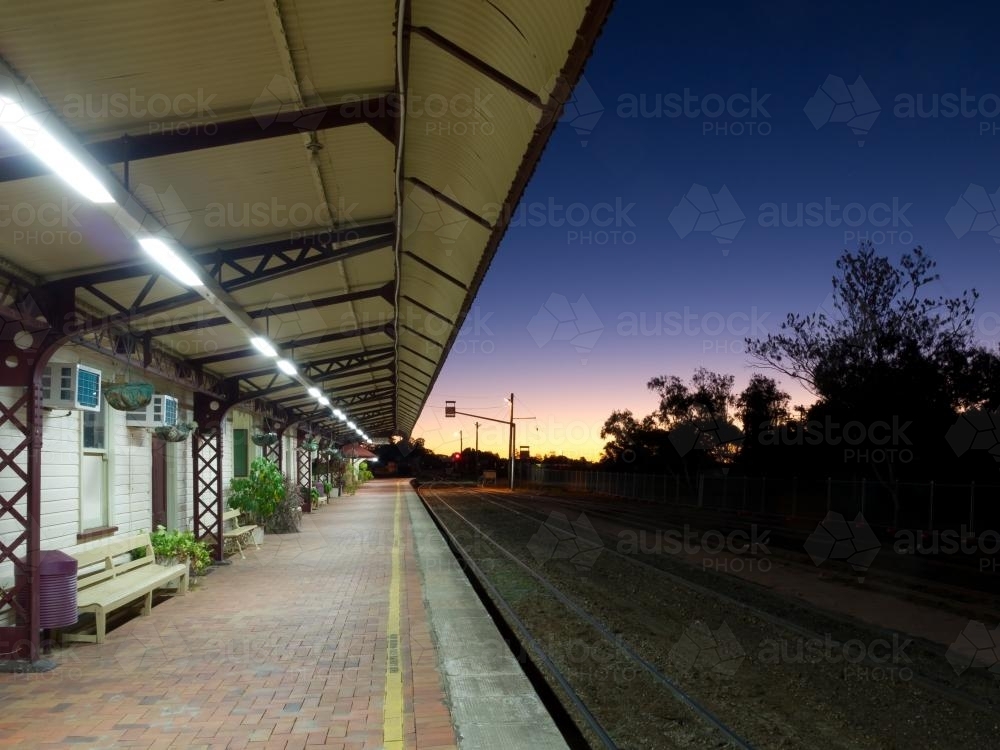 Looking along lighted railway station platform at dusk - Australian Stock Image