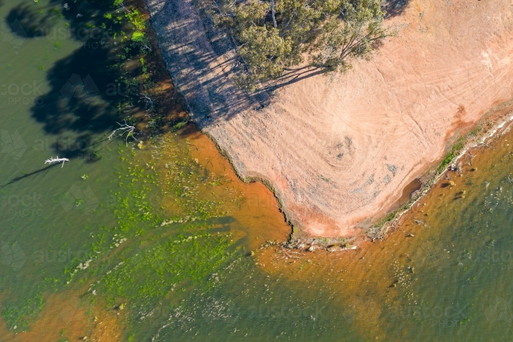 Looking down on a dry dirt beach covered with wheel tracks and surrounded by brackish water. - Australian Stock Image