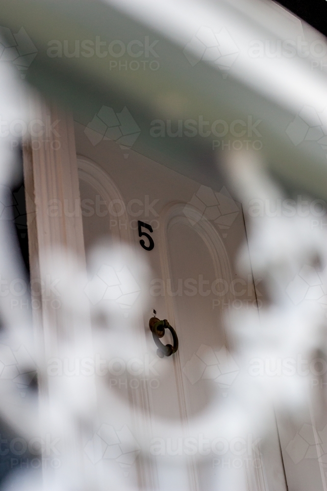 Looking past a cast iron decorative balustrade to a exterior house door with number 5 - Australian Stock Image
