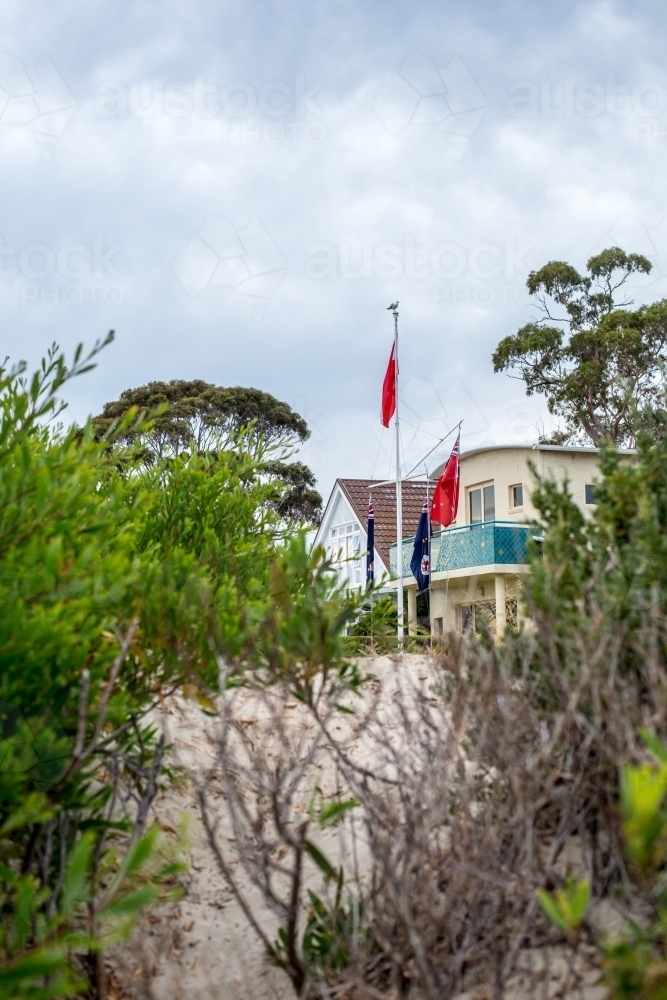 Looking through beach shrubs to a beach house and flag pole - Australian Stock Image