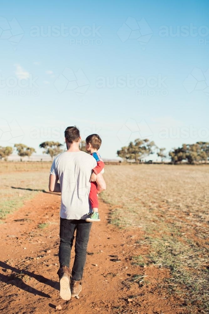 Man holding toddler walking in a paddock - Australian Stock Image
