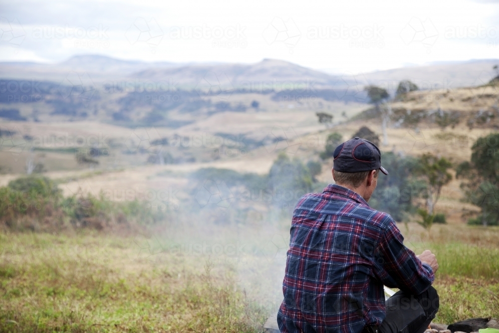 Man sitting in front of fire pit looking over his farm - Australian Stock Image