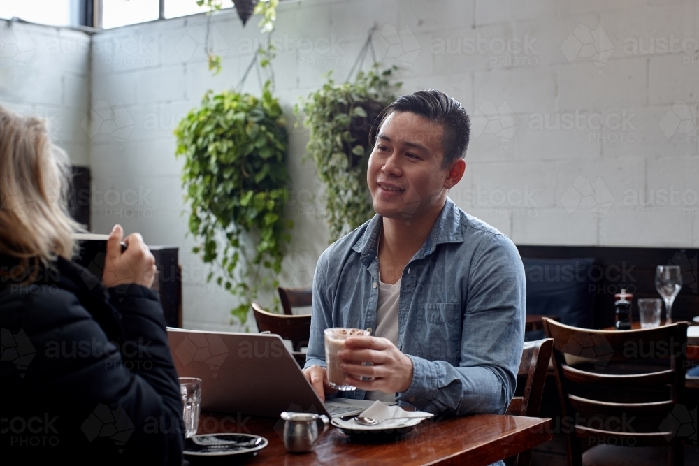 Man talking with friend whilst drinking coffee at cafe - Australian Stock Image