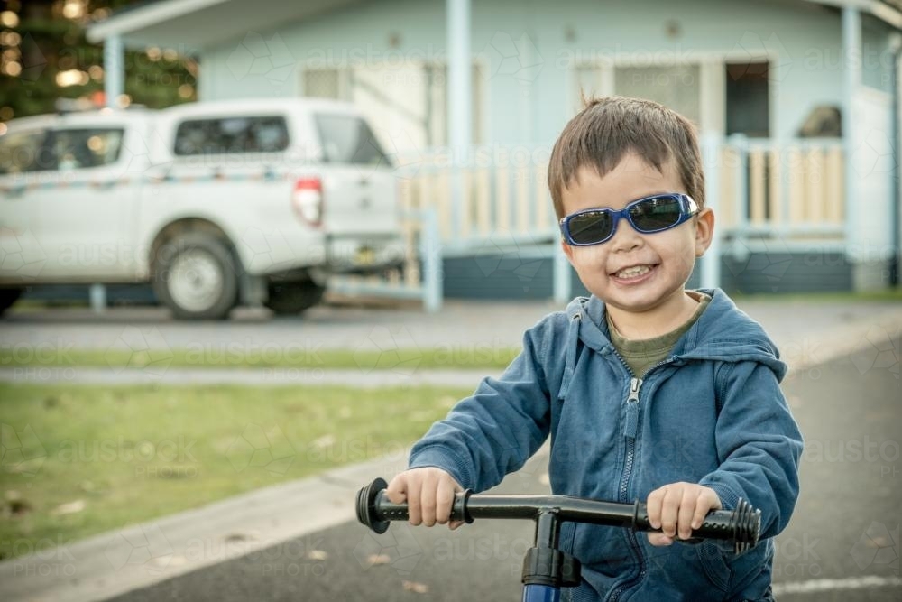 Mixed race boy wearing sunglasses and riding his bike in a coastal NSW holiday park - Australian Stock Image